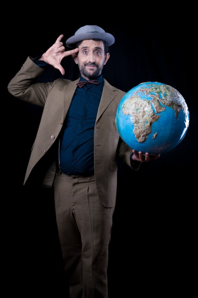 man in brown suit jacket and dress pants holding planet earth toy